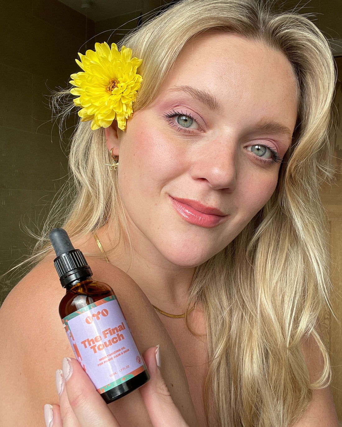 Woman with flower in hair holds 'The Final Touch' natural skincare oil, promoting irritation-free, nourishing skin.