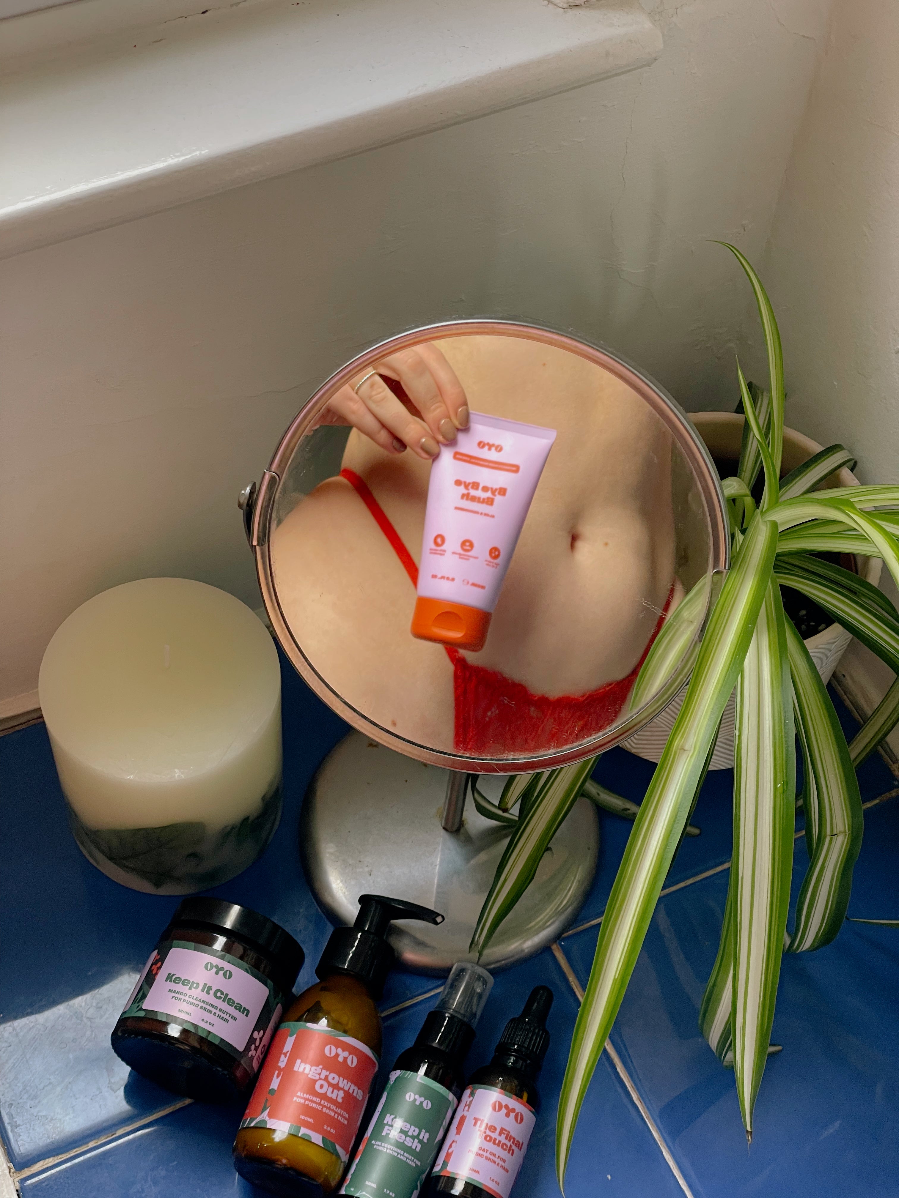 Woman holding natural skincare product reflecting in a mirror, surrounded by plant and candles, promoting effective, safe skincare.