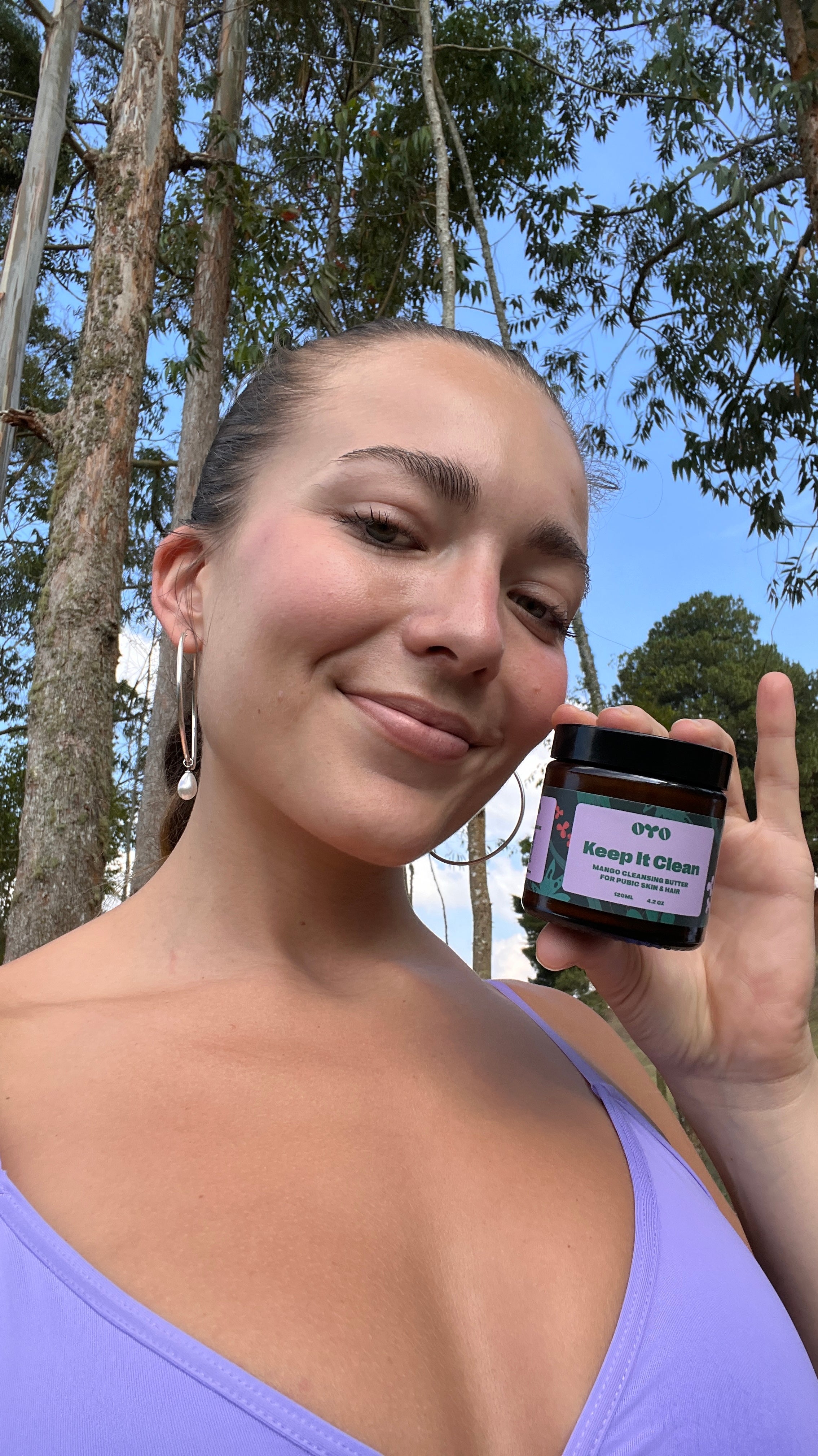 Woman holding natural skincare product 'Keep It Clean' in a lush setting, showcasing effective skincare for all skin types.